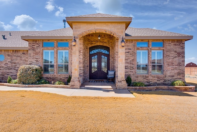 doorway to property with french doors, brick siding, and roof with shingles