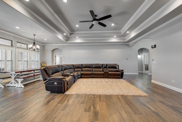 living area featuring arched walkways, dark wood finished floors, a tray ceiling, and ornamental molding