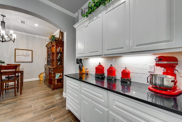 kitchen with visible vents, ornamental molding, backsplash, wood finished floors, and arched walkways