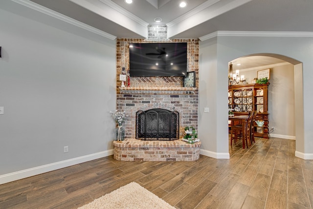 living room with wood finished floors, baseboards, a fireplace, arched walkways, and ornamental molding