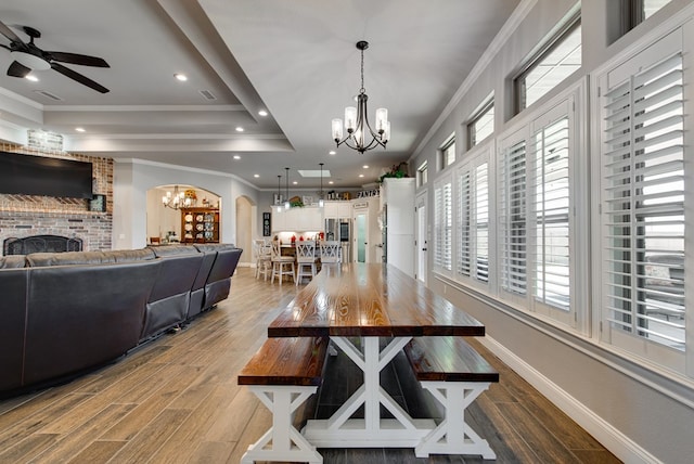 dining space featuring wood finished floors, baseboards, a tray ceiling, arched walkways, and ornamental molding