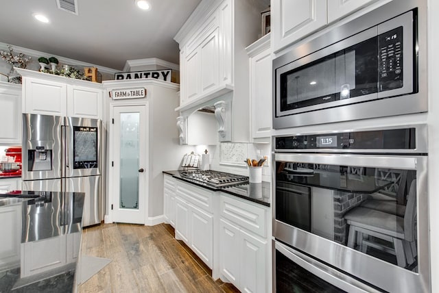 kitchen featuring visible vents, dark countertops, wood finished floors, stainless steel appliances, and crown molding