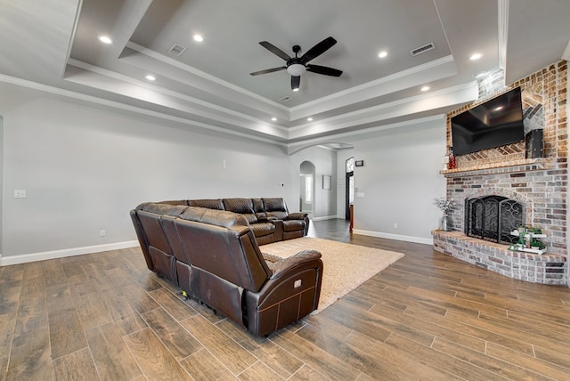 living area with a tray ceiling, arched walkways, visible vents, and wood finished floors