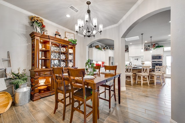 dining room with crown molding, arched walkways, visible vents, and wood tiled floor