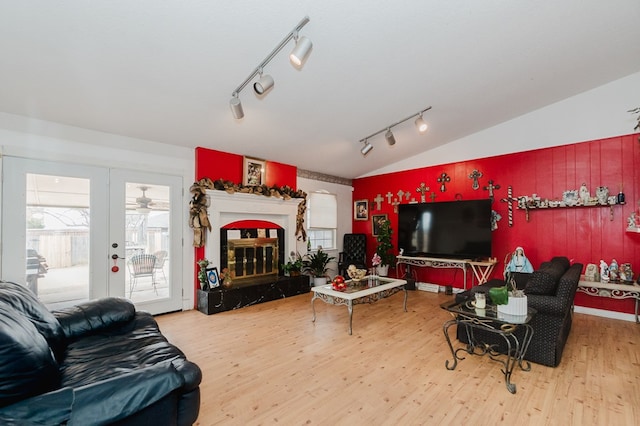 living room with a wealth of natural light, vaulted ceiling, wood finished floors, and a glass covered fireplace