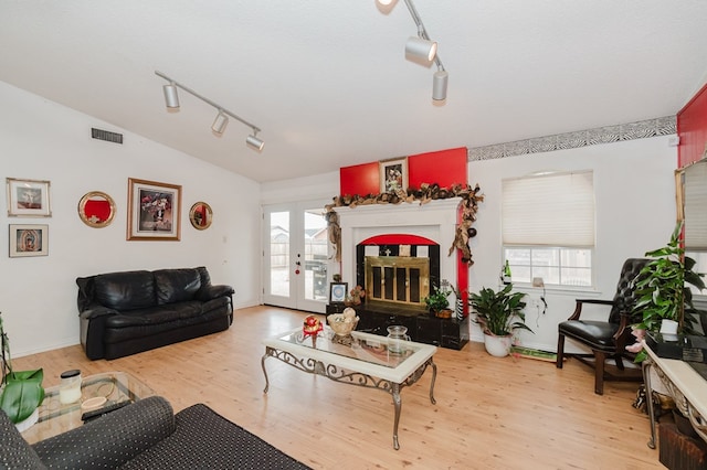 living room with visible vents, a glass covered fireplace, wood finished floors, vaulted ceiling, and french doors