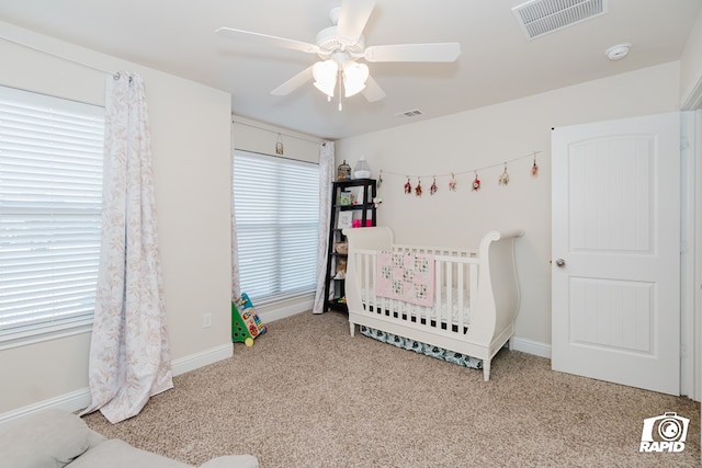 carpeted bedroom with multiple windows, a nursery area, and ceiling fan