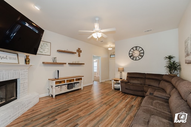 living room with ceiling fan, hardwood / wood-style floors, and a brick fireplace