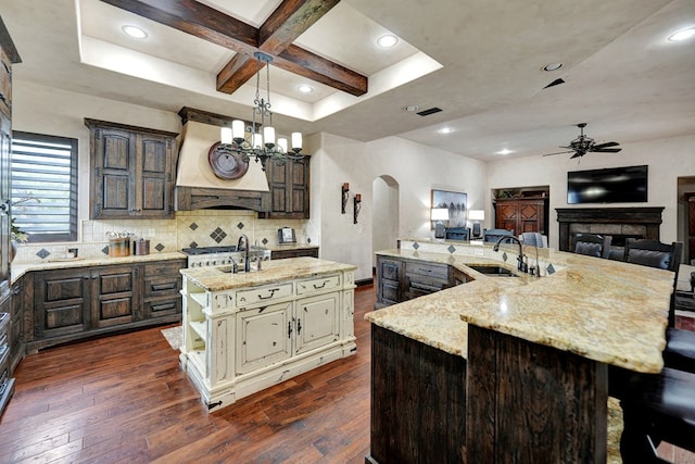 kitchen with a large island with sink, a sink, ceiling fan, cream cabinets, and arched walkways