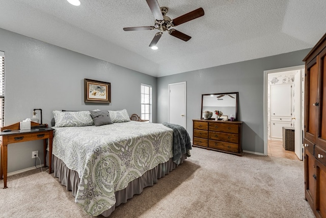 bedroom with ceiling fan, light colored carpet, ensuite bathroom, and a textured ceiling