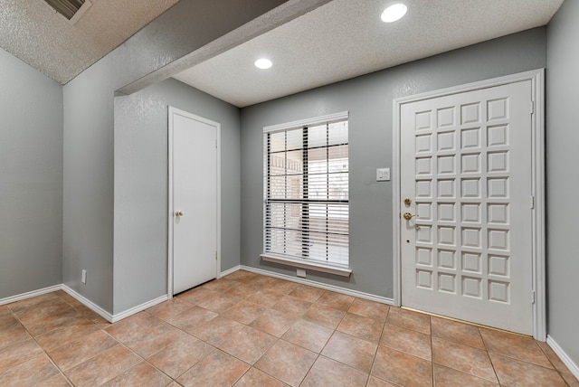 foyer entrance with a textured ceiling and light tile patterned floors