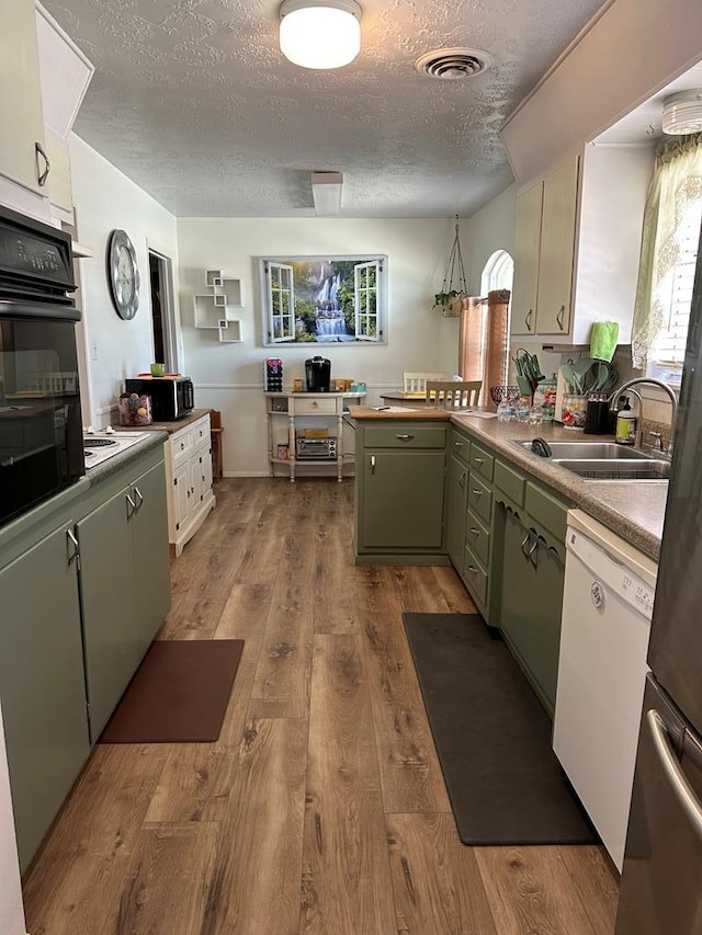 kitchen with visible vents, a sink, black oven, wood finished floors, and white dishwasher