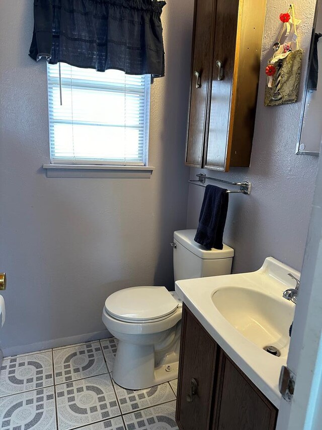 half bathroom with tile patterned flooring, toilet, vanity, and baseboards