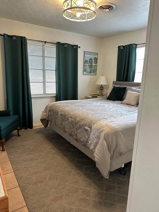 carpeted bedroom with tile patterned floors, visible vents, and a textured ceiling