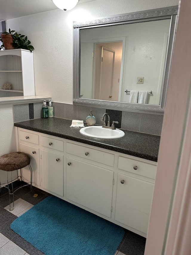 bathroom featuring vanity, granite finish floor, a textured wall, and backsplash