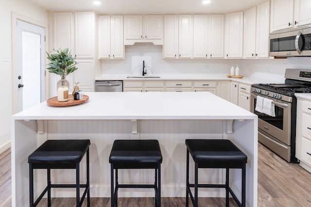 kitchen featuring tasteful backsplash, white cabinets, appliances with stainless steel finishes, light wood-style floors, and a sink