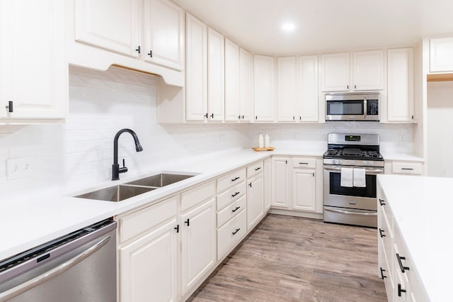 kitchen with light countertops, light wood-style flooring, appliances with stainless steel finishes, white cabinetry, and a sink