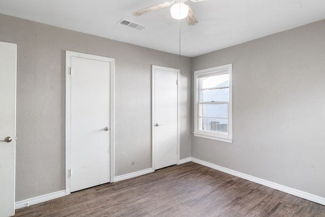 unfurnished bedroom with dark wood-style floors, visible vents, baseboards, and a ceiling fan