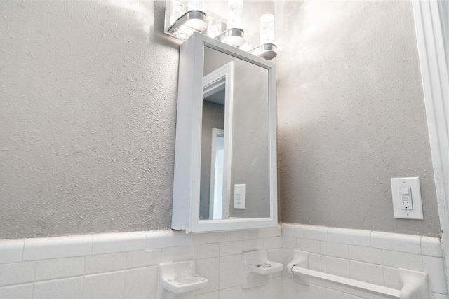 bathroom featuring a wainscoted wall, a textured wall, and tile walls