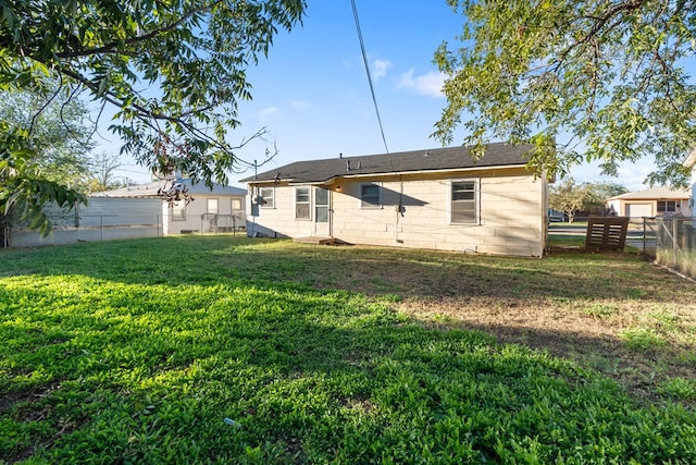 rear view of house with a lawn, concrete block siding, and a fenced backyard