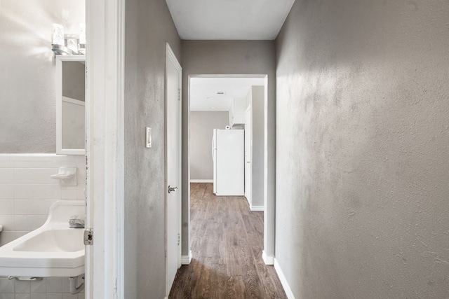 corridor featuring a textured wall, a sink, tile walls, and wood finished floors