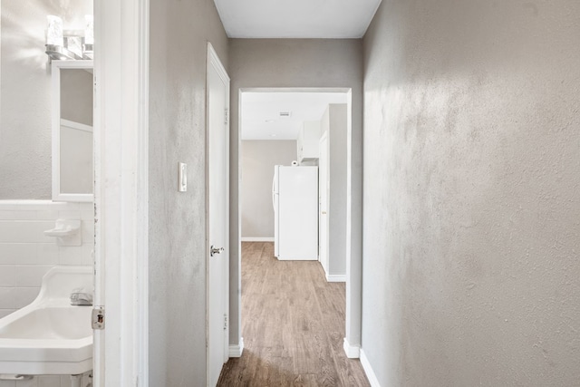 corridor with a textured wall, light wood-type flooring, and a sink