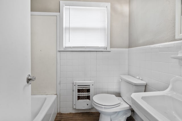 bathroom with toilet, a bathing tub, wood finished floors, heating unit, and tile walls