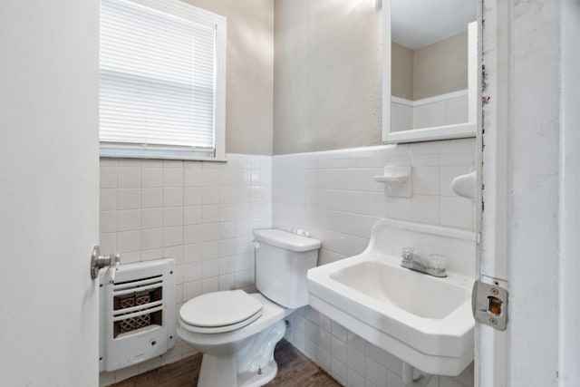 half bathroom featuring toilet, wood finished floors, tile walls, a sink, and heating unit