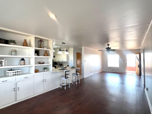 kitchen featuring dark hardwood / wood-style flooring, ceiling fan, decorative light fixtures, white cabinets, and a breakfast bar area