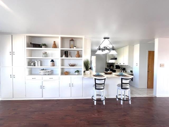 kitchen featuring a breakfast bar, decorative light fixtures, white cabinetry, and dark hardwood / wood-style floors