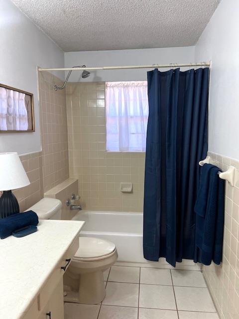 full bathroom featuring shower / bath combo, tile patterned floors, toilet, vanity, and tile walls