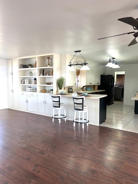 kitchen featuring black refrigerator, decorative light fixtures, white cabinetry, kitchen peninsula, and a breakfast bar area