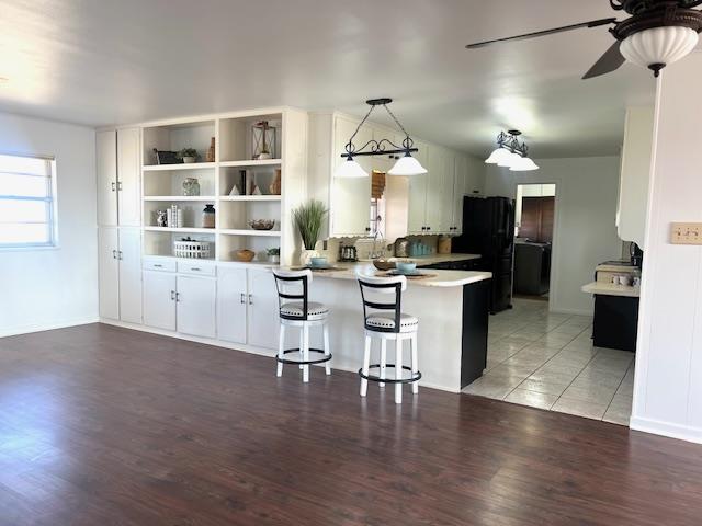 kitchen with kitchen peninsula, white cabinetry, black refrigerator, and a breakfast bar