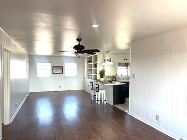 unfurnished living room with built in shelves, ceiling fan, and dark wood-type flooring