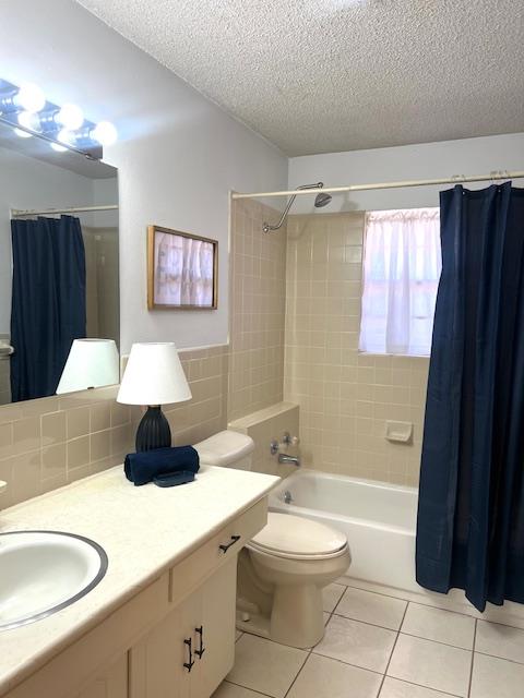 full bathroom featuring vanity, tile patterned flooring, toilet, shower / bath combo with shower curtain, and a textured ceiling