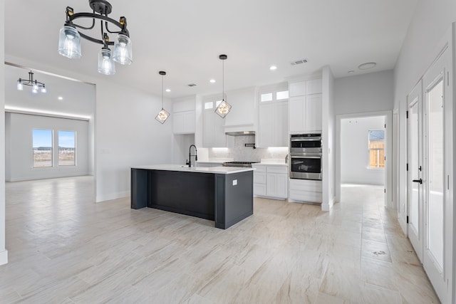 kitchen featuring sink, decorative light fixtures, stainless steel appliances, a kitchen island with sink, and white cabinets