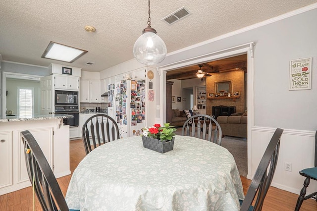 4704 Elma Dr, Midland, TX 79707 - dining space featuring a brick fireplace, light wood-style floors, a textured ceiling, ceiling fan, and crown molding