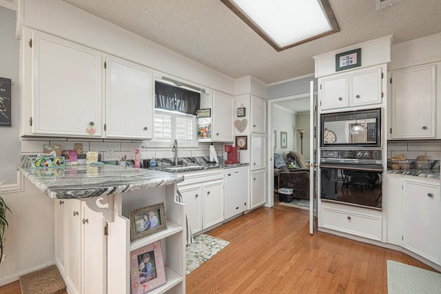 4704 Elma Dr, Midland, TX 79707 - kitchen featuring black appliances, a textured ceiling, white cabinets, light wood finished floors, and backsplash