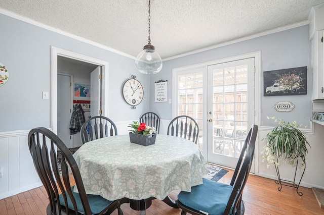 4704 Elma Dr, Midland, TX 79707 - dining area featuring a textured ceiling, light wood-style flooring, crown molding, wainscoting, and a decorative wall