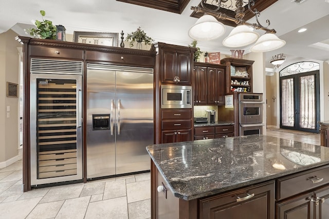 kitchen featuring dark brown cabinetry, beverage cooler, built in appliances, decorative light fixtures, and a center island