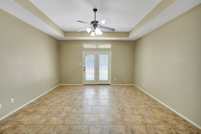 empty room with light tile patterned floors, baseboards, a raised ceiling, and ceiling fan