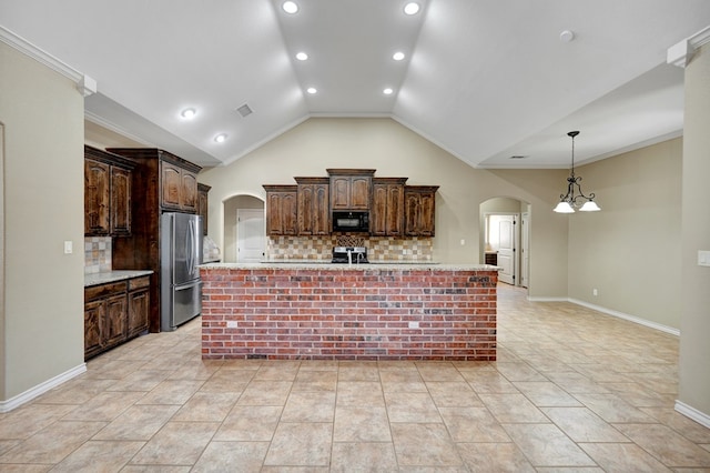 kitchen with stove, black microwave, a large island with sink, freestanding refrigerator, and arched walkways