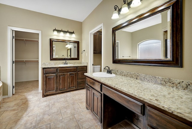 bathroom with a sink, a walk in closet, baseboards, and two vanities