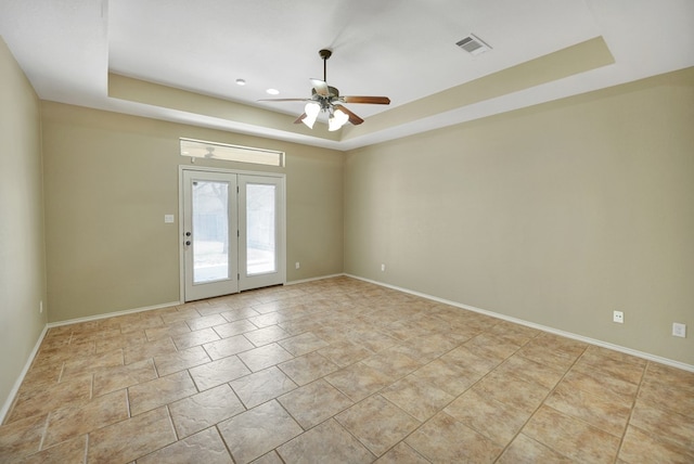 spare room with a tray ceiling, a ceiling fan, visible vents, and baseboards