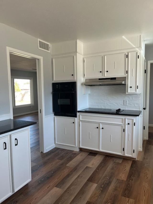 kitchen with dark countertops, visible vents, dark wood-type flooring, under cabinet range hood, and black appliances