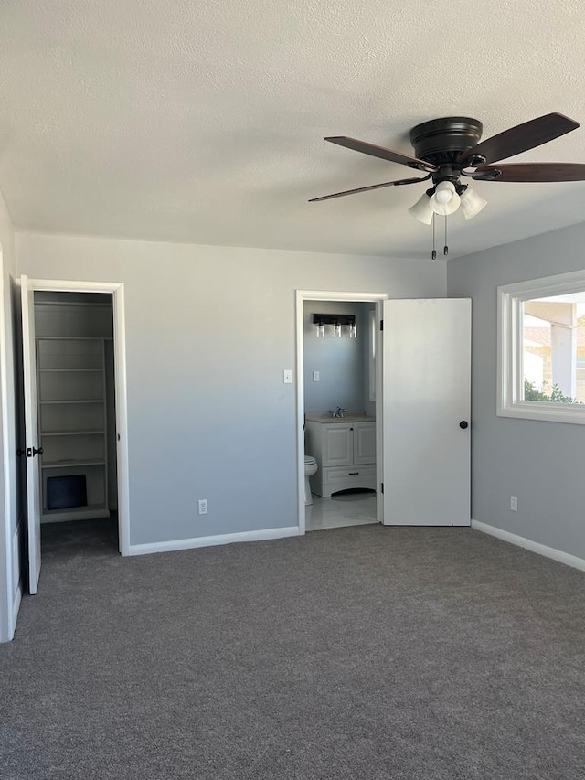 unfurnished bedroom featuring ensuite bath, carpet, baseboards, and a textured ceiling