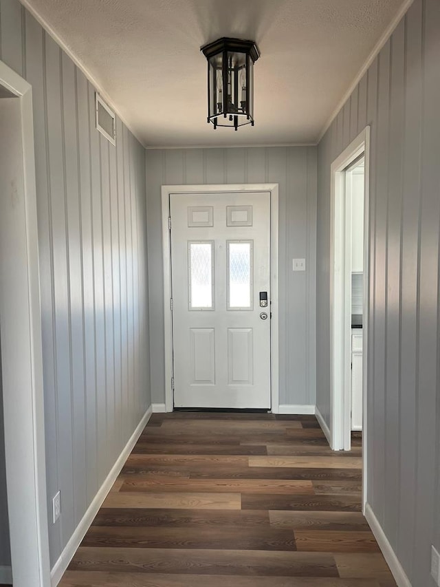 doorway to outside with a notable chandelier, dark wood finished floors, visible vents, and baseboards