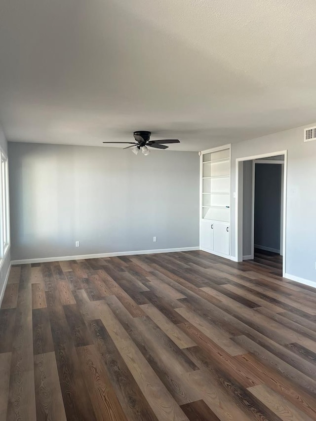 unfurnished room with dark wood-type flooring, visible vents, ceiling fan, and baseboards