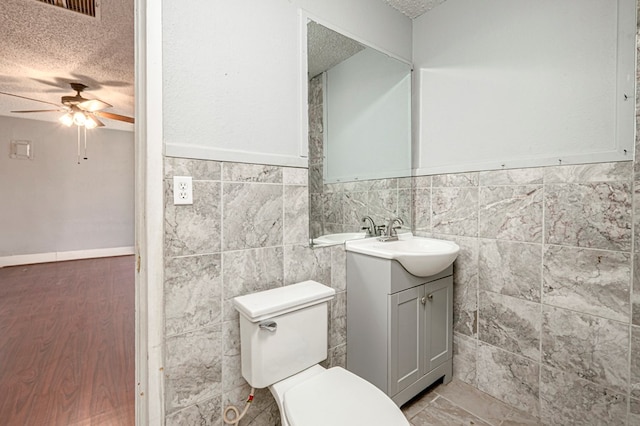 3608 S County Rd 1195, Midland, TX 79706 - half bathroom with a textured ceiling, ceiling fan, tile walls, vanity, and wainscoting