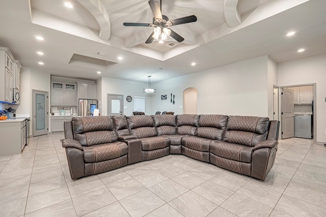 tiled living room with ceiling fan and a tray ceiling